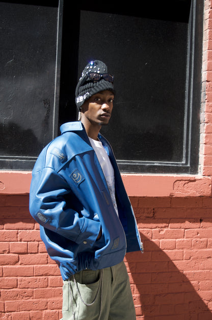 Person wearing a blue jacket and hat standing against a brick wall with a window.